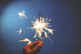 A hand holds up a lit sparkler firework.