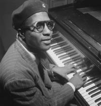 A jazz piano player looks at the camera while playing a piano.