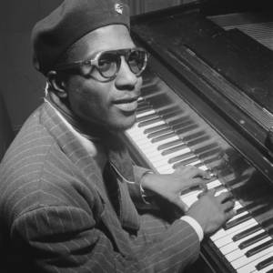 A jazz piano player looks at the camera while playing a piano.