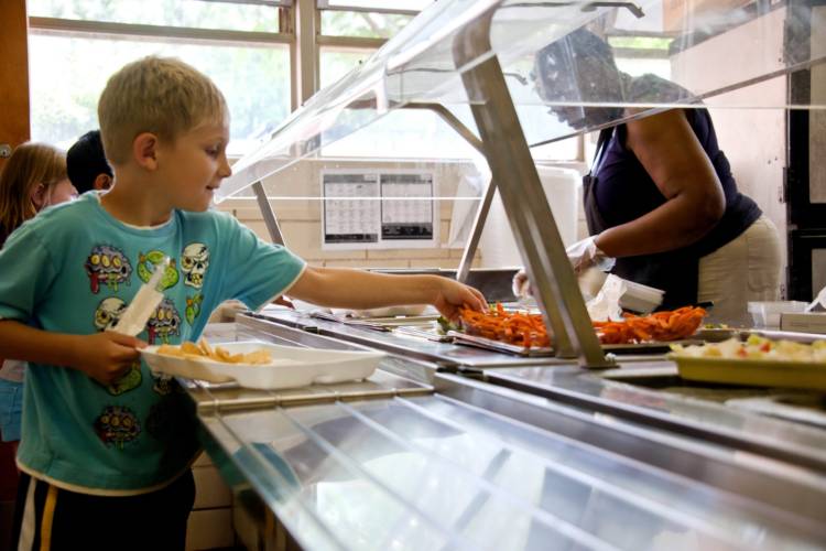 A child slides a tray through a school lunch line, taking food.