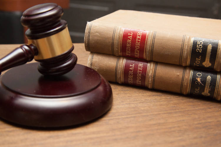 A wooden gavel sits next to two law books on a desk.