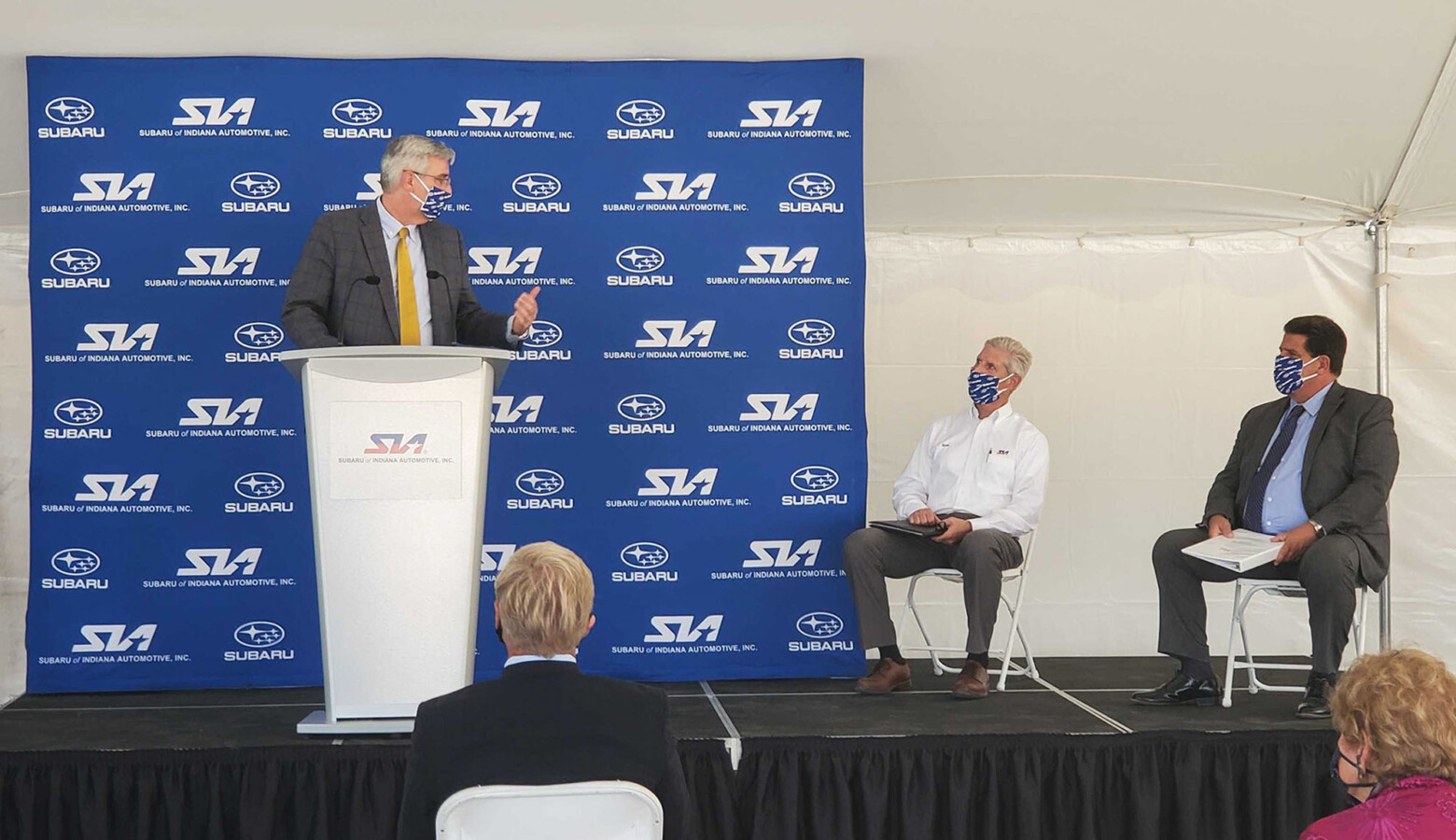 (Left to right) Gov. Eric Holcomb speaks at Subaru of Indiana Automotive ground breaking with SIA Vice President Scott Brand and Lafayette Mayor Tony Roswarski sitting on stage. (Samantha Horton/IPB News)