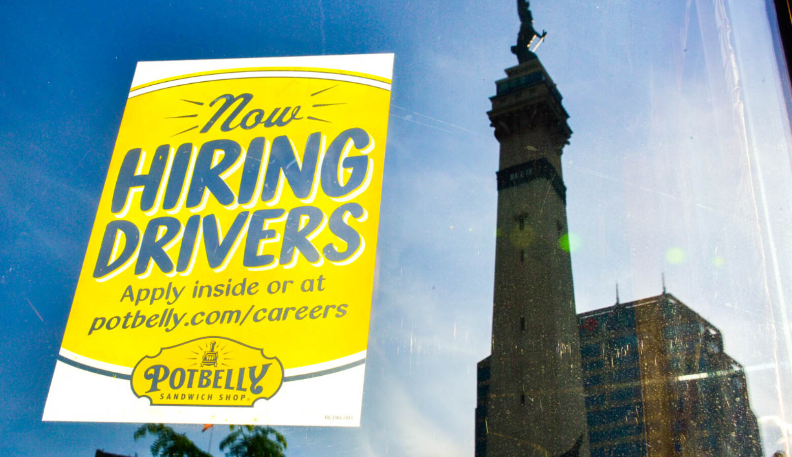 A hiring sign on the window of a sandwich shop with the reflection of the Indiana State Soldiers and Sailors Monument in the background. (Justin Hicks/IPB News)