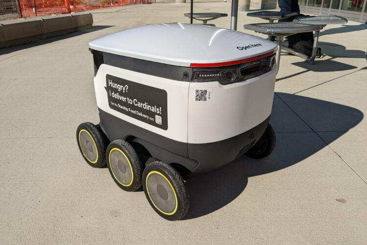 A delivery robot that's white in color, with six wheels.