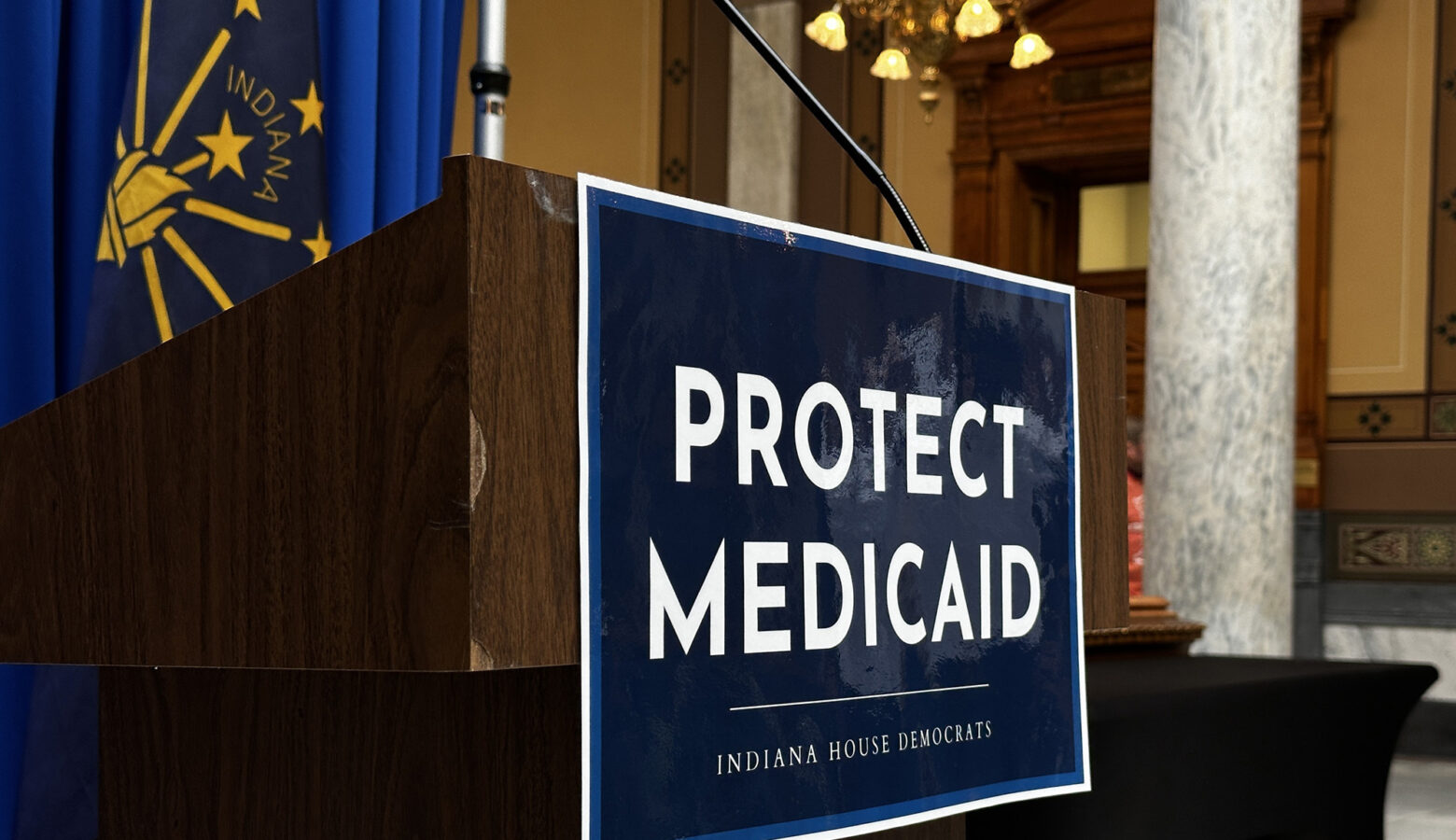 An empty podium has a sign taped to it that reads Protect Medicaid and Indiana House Democrats.
