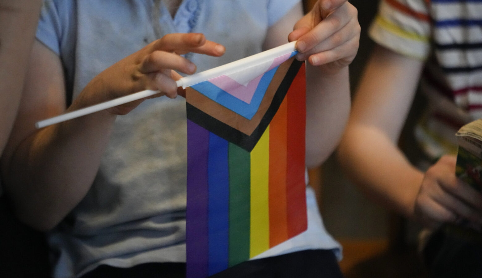 A person holds a small version of the Progressive Pride flag.