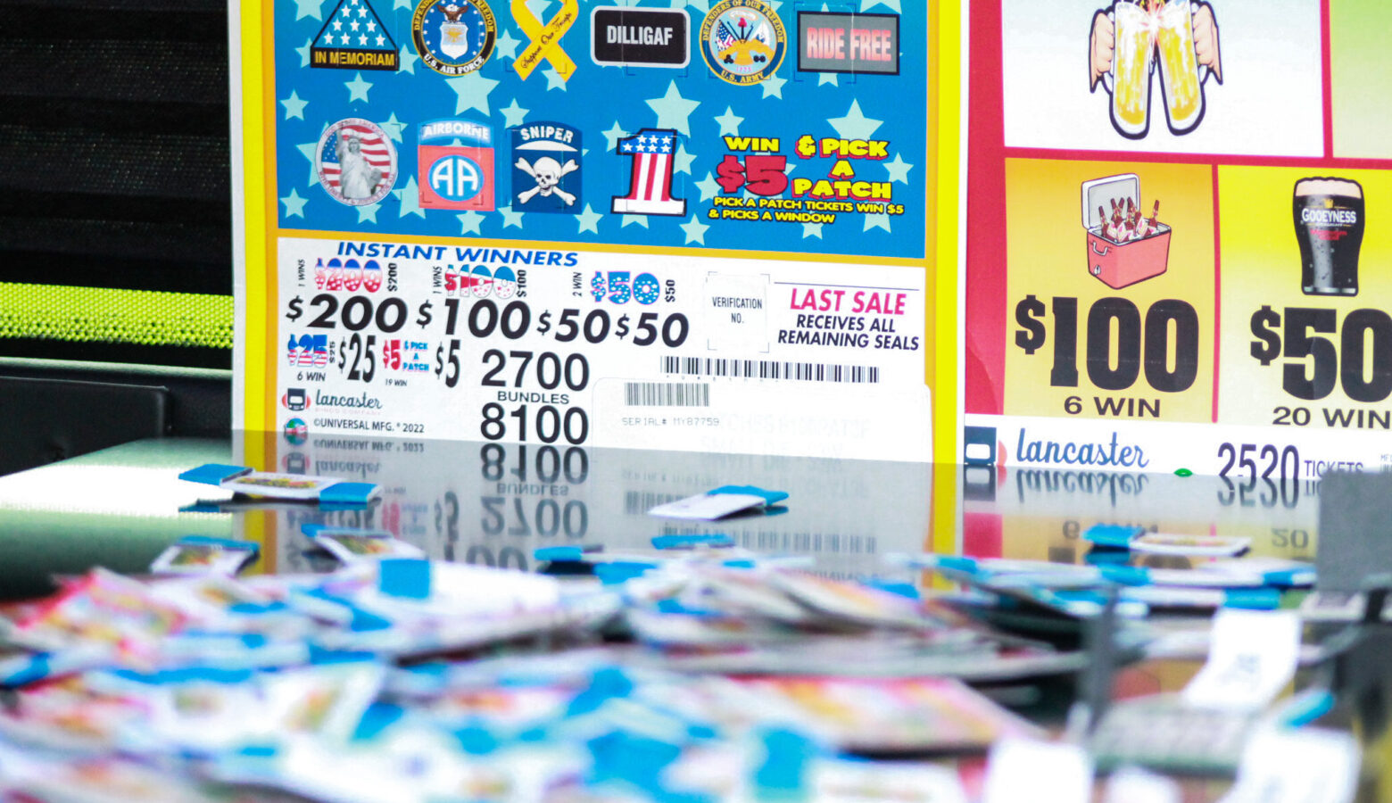 Strips of multi-colored paper are strewn across a table top in the foreground, out of focus. In the background are signs displaying prize amounts for pull tab charity games.