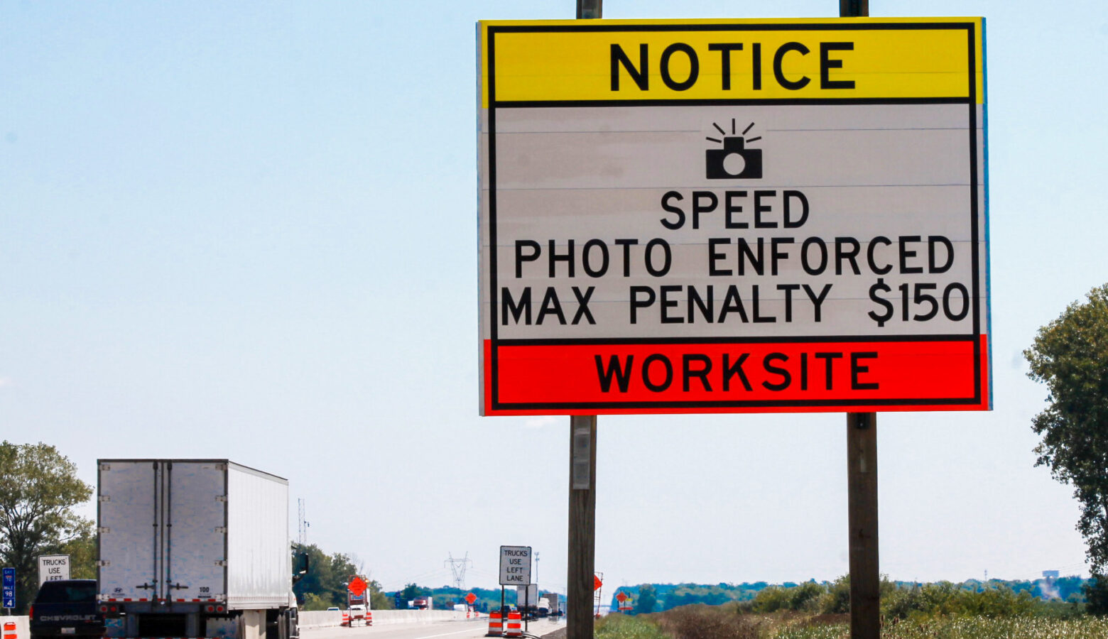 A highway sign reads "Notice Speed Photo Enforced Max Penalty $150 Worksite"