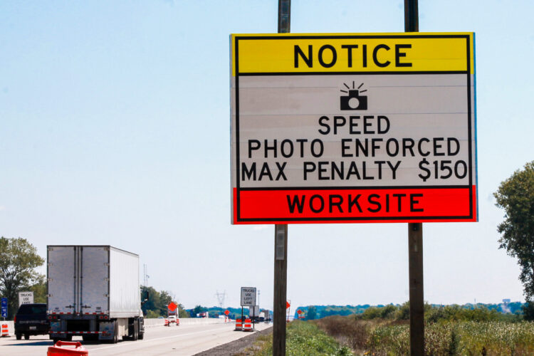 A highway sign reads "Notice Speed Photo Enforced Max Penalty $150 Worksite"