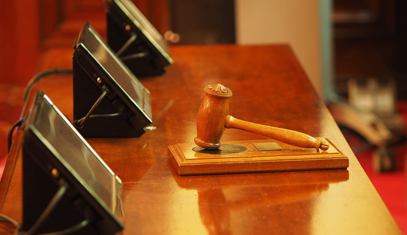 A gavel resting on a table with three screens on it.