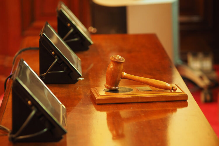 A gavel resting on a table with three screens on it.