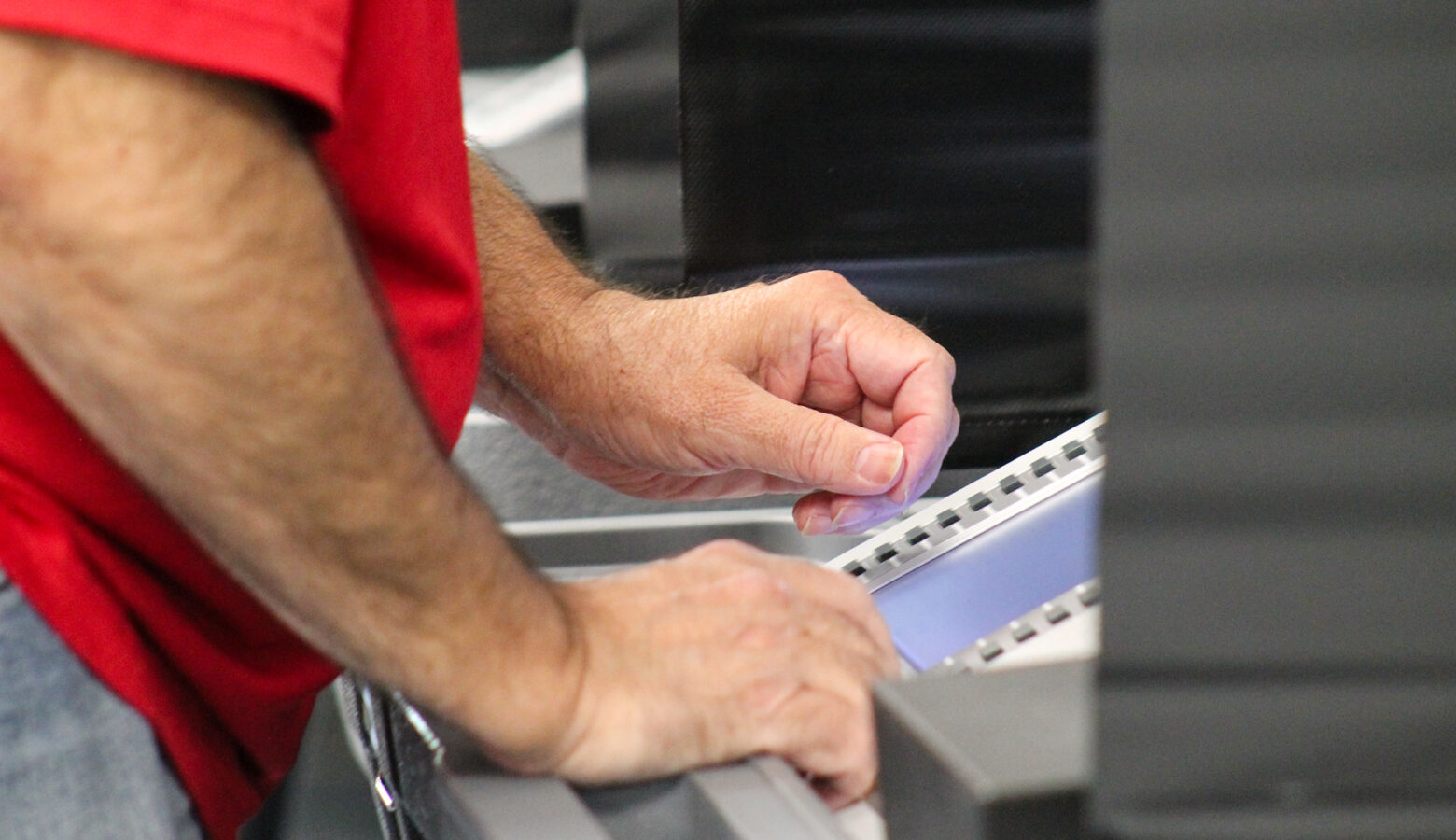 A side-on view of a person using a voting machine at a polling place. Only the person's arms, hands and midsection are visible, along with the machine, though its screen isn't readable.