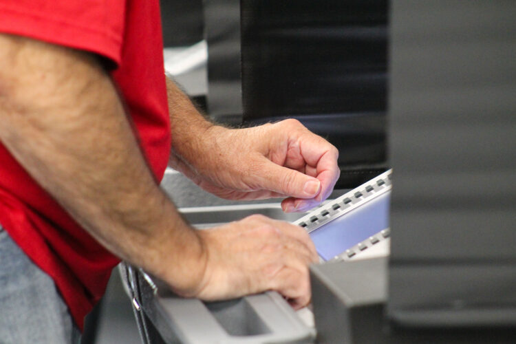 A side-on view of a person using a voting machine at a polling place. Only the person's arms, hands and midsection are visible, along with the machine, though its screen isn't readable.