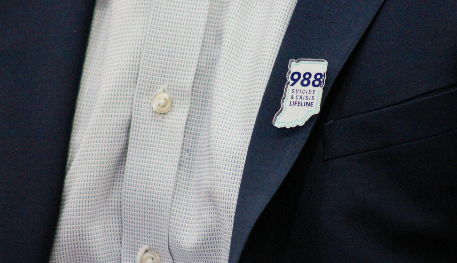 A person wearing a suit with a 988 pin, in the shape of the state of Indiana, on the lapel.