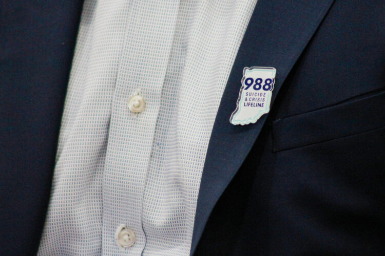 A person wearing a suit with a 988 pin, in the shape of the state of Indiana, on the lapel.