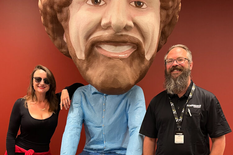 A woman and a man pose next to a large statue of Bob Ross at the IPR Studios.