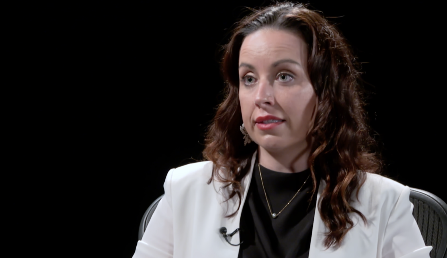 A screenshot from a video interview with Destiny Wells. Wells is a White woman with dark brown hair. She is wearing a white jacket over a black top.