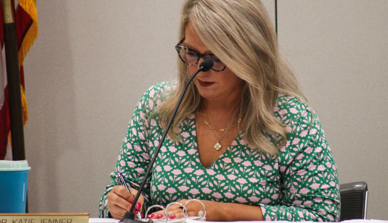 Katie Jenner writes on a piece of paper while sitting in front of a microphone.