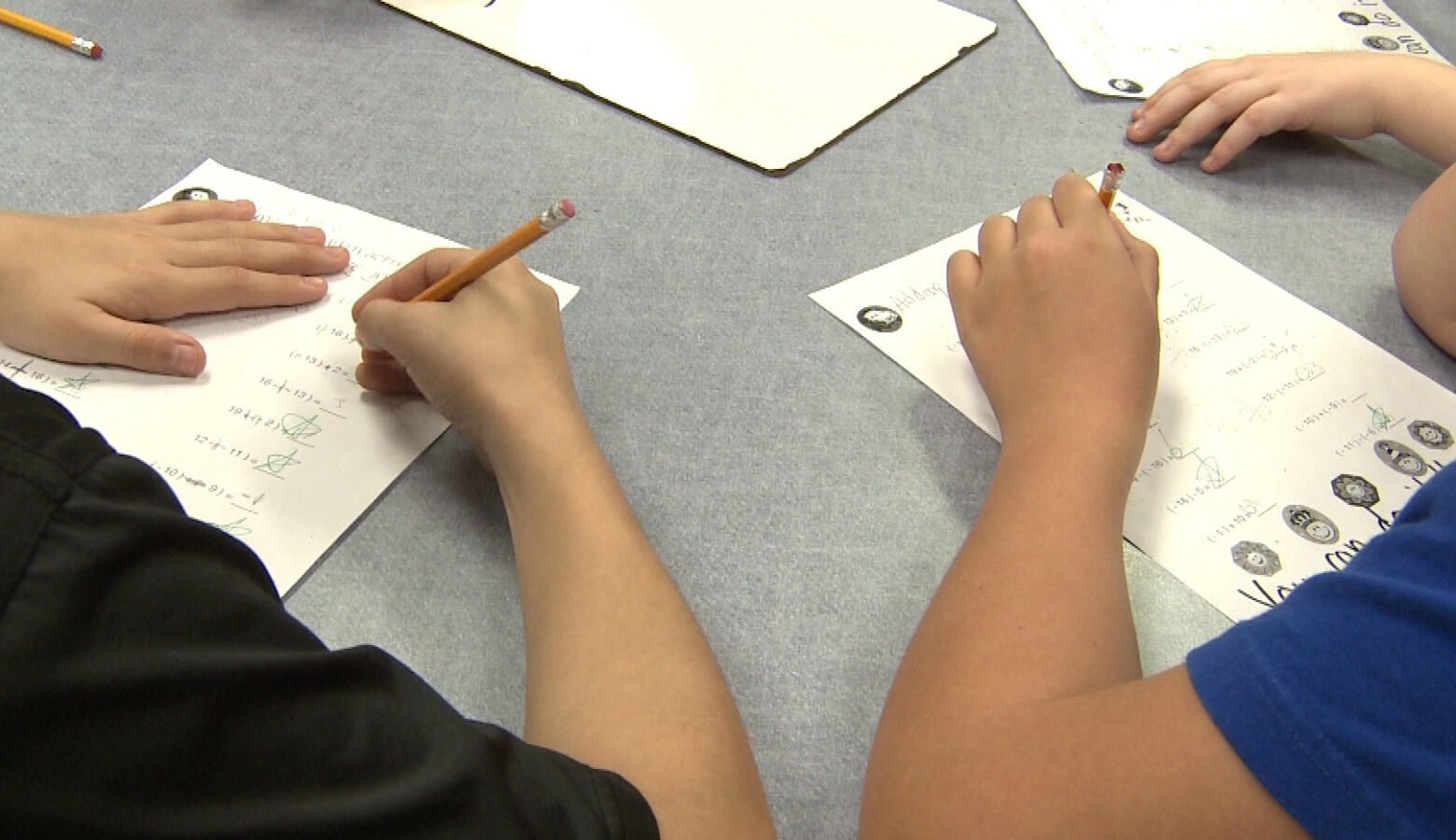 Two students sit at a table and answer math problems.