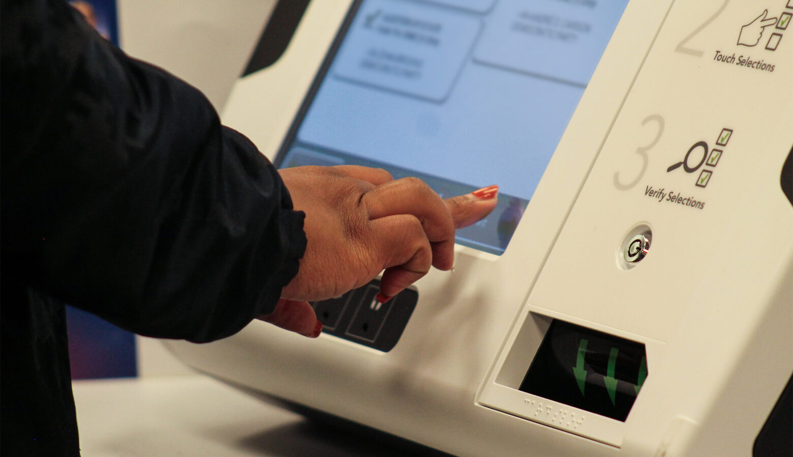 A voter's hand is about to press a button on a voting machine.