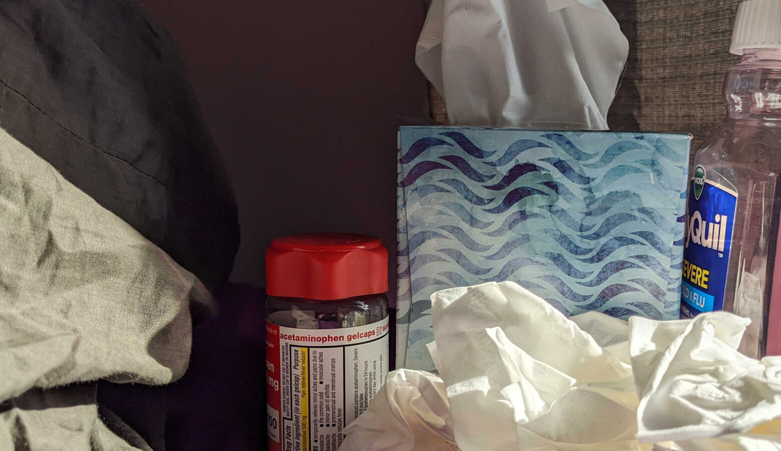 A pile of tissues sits next to a tissue box with cold medicines surrounding it.