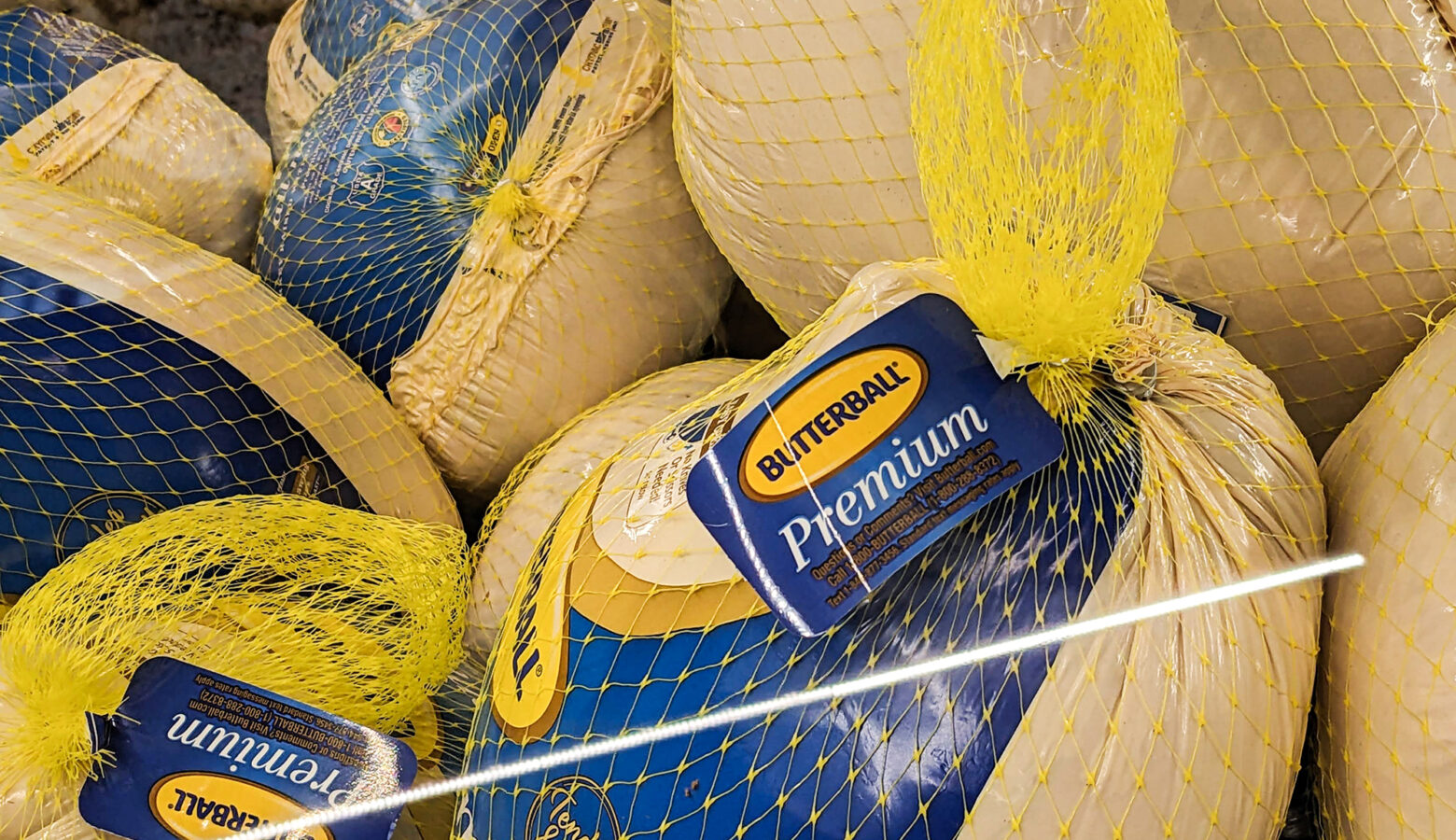 A freezer case at a grocery store is filled with frozen processed turkeys.