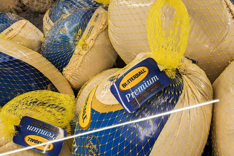 A freezer case at a grocery store is filled with frozen processed turkeys.