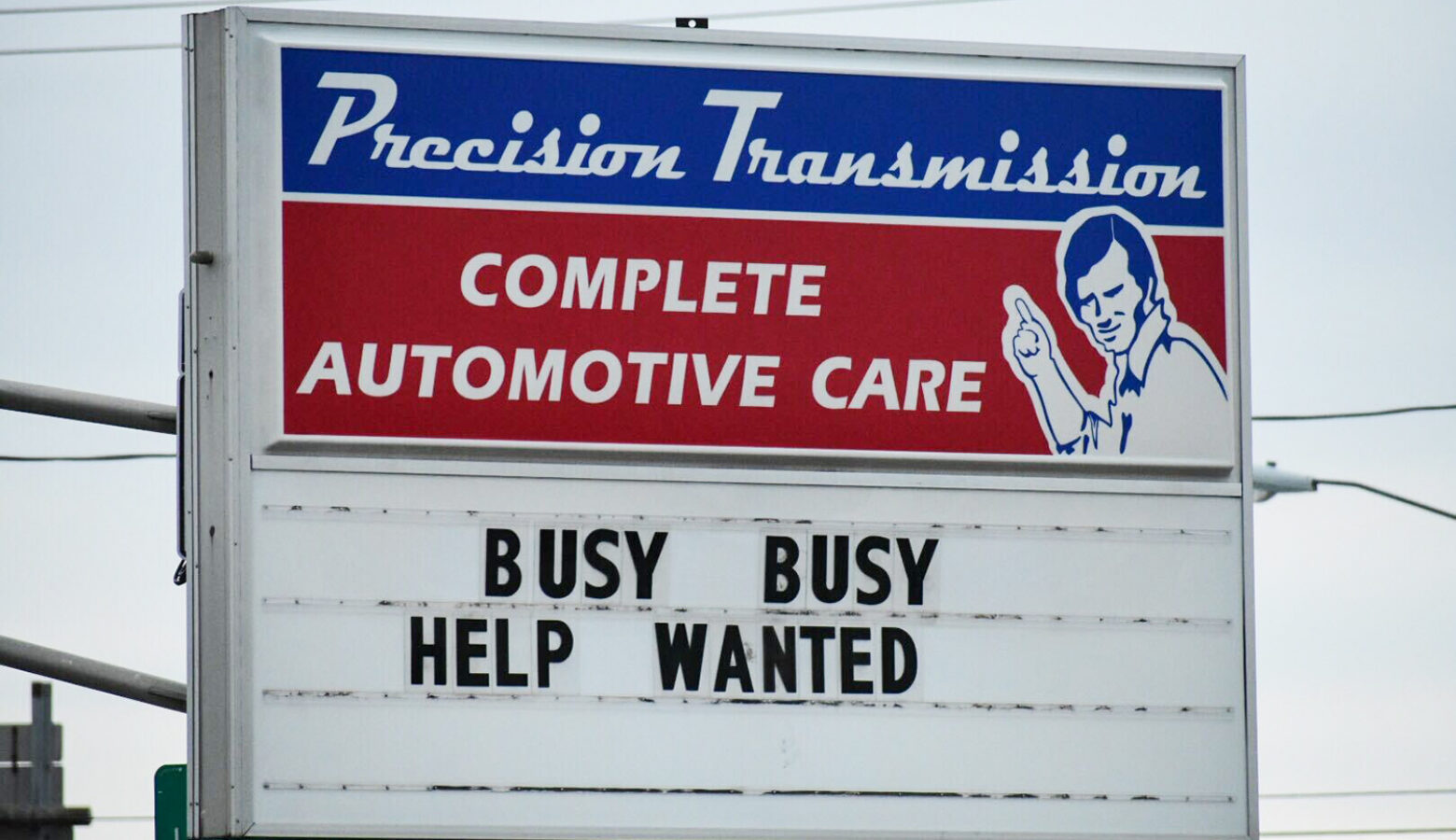 A sign reads "Precision Transmission, complete automotive care." Below the business' logo are the words "Busy busy help wanted."