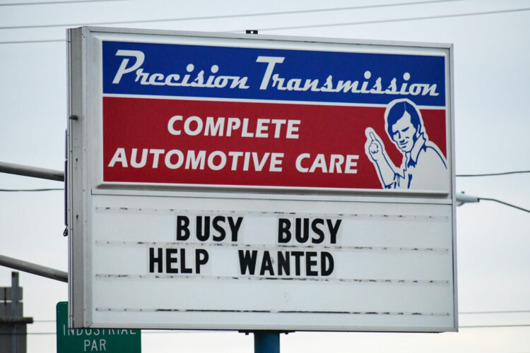 A sign reads "Precision Transmission, complete automotive care." Below the business' logo are the words "Busy busy help wanted."