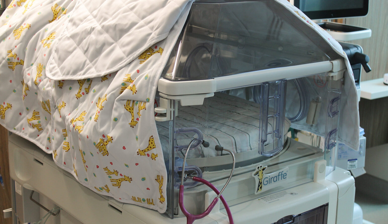 A baby hospital bed covered by a baby blanket with giraffes on it.