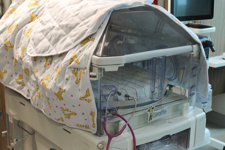 A baby hospital bed covered by a baby blanket with giraffes on it.