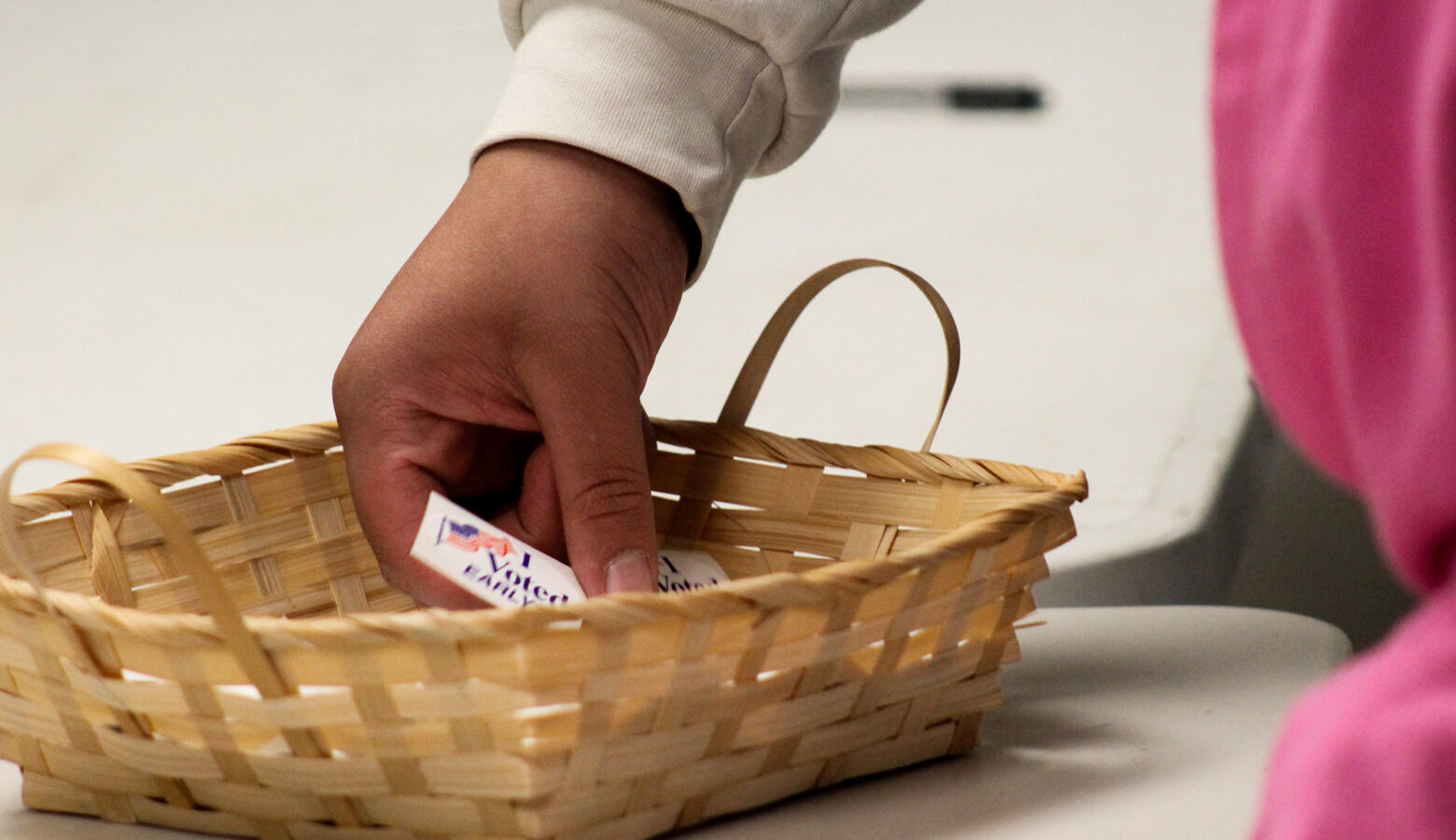 Stickers in a basket are picked through by a voter. The one visible says 'I voted early'