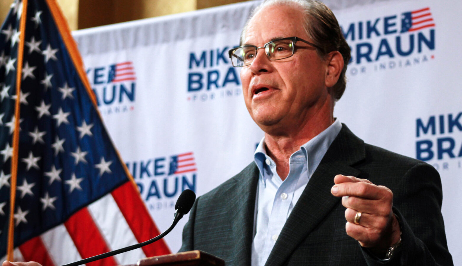 Mike Braun stands at a podium with his campaign logo on a screen behind him.