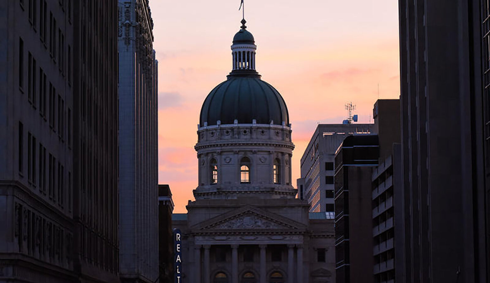 The Indiana Statehouse at sunset, framed between neighboring buildings.