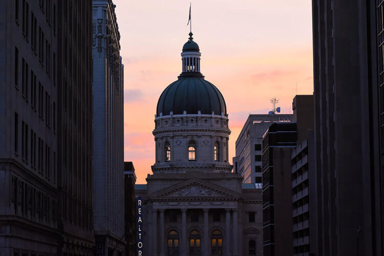 The Indiana Statehouse at sunset, framed between neighboring buildings.