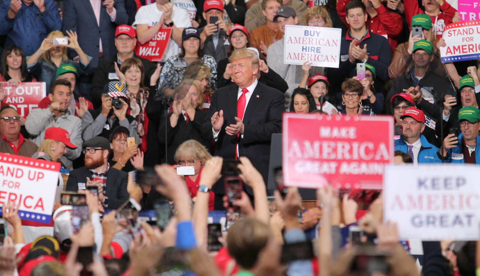 Donald Trump speaks at a rally in Indianapolis. He is surrounded by a crowd holding 'Make America Great Again' signs and cheering for him.