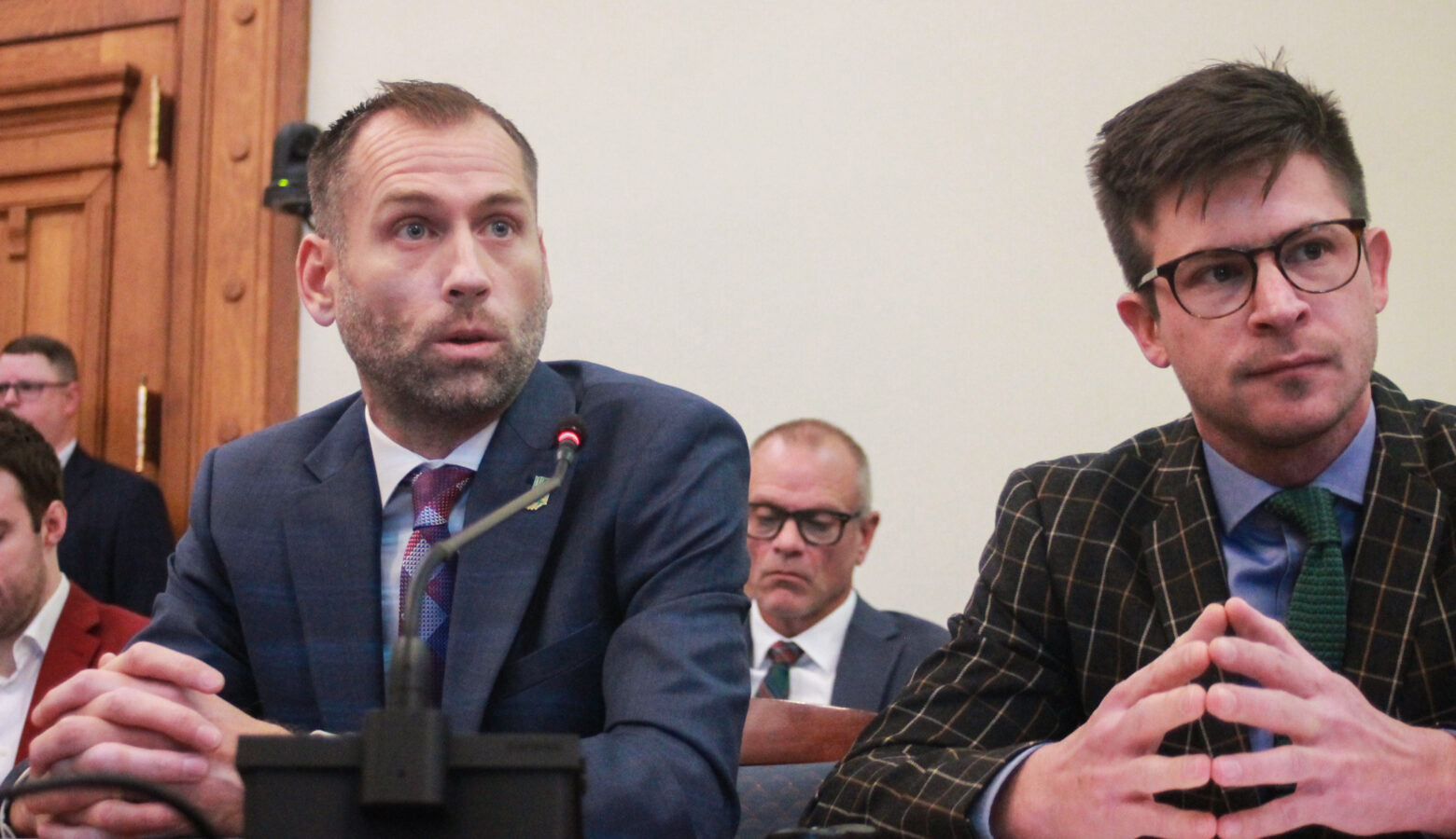 Brock Herr and Mark Wasky sit at a desk, with a microphone between them. Herr is a White man, balding with dark, graying hair and beard. Wasky is a White man with dark hair and wearing glasses.