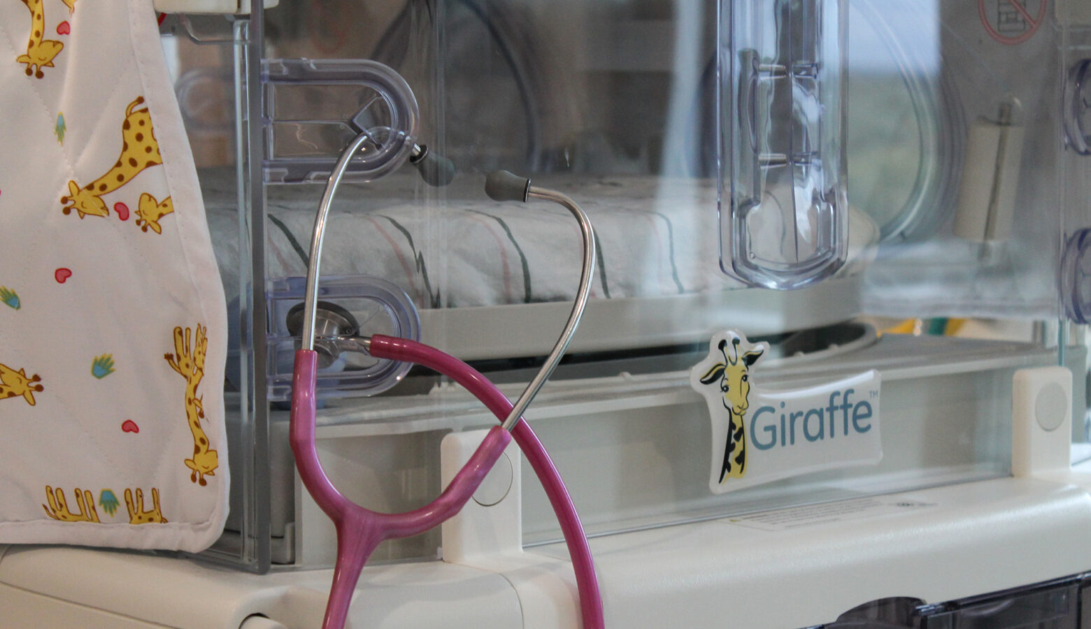 A pink stethoscope hangs on a part of a baby omnibed in a hospital.