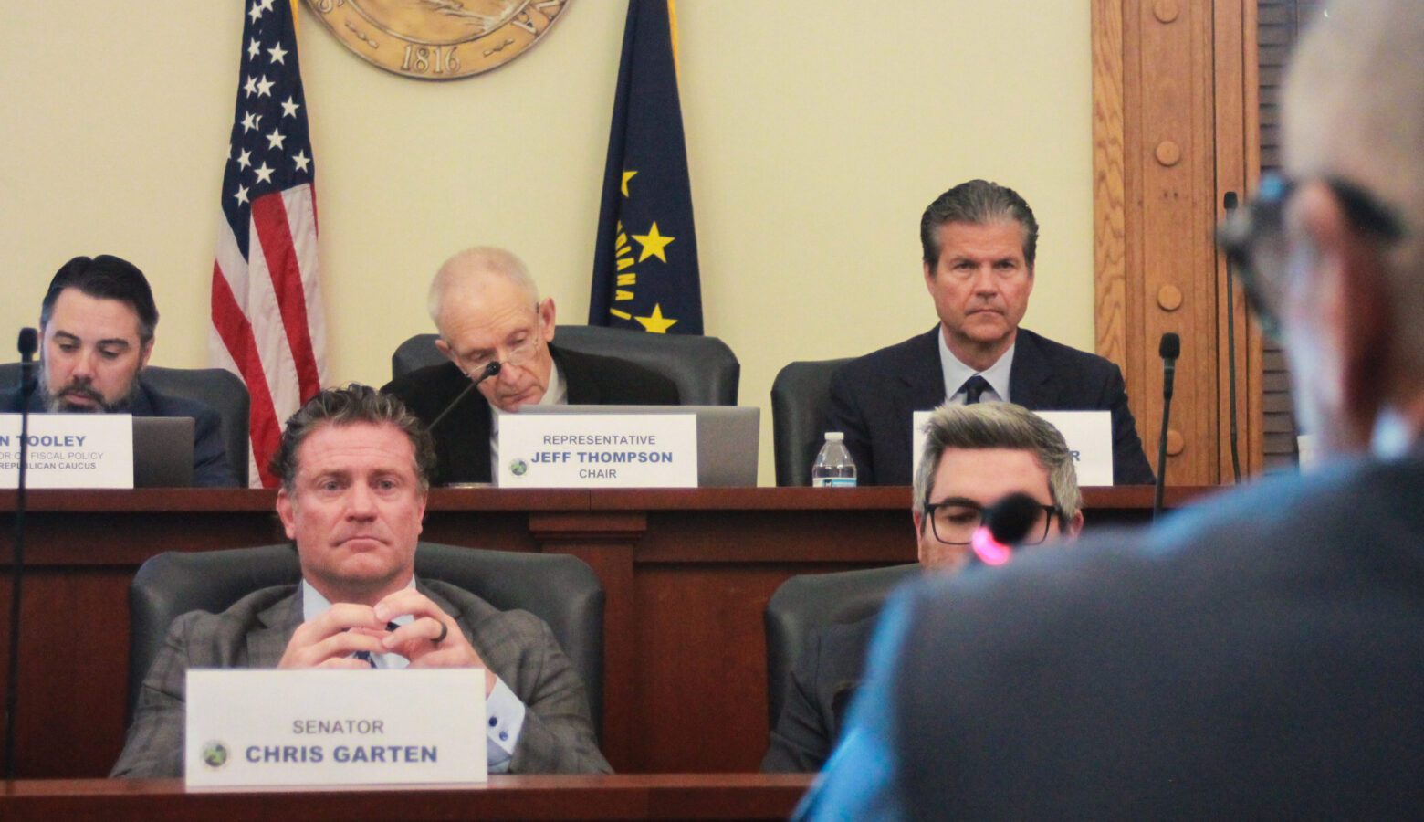 Lawmakers sit in their chairs on two tiers of desks, watching someone speak to them.