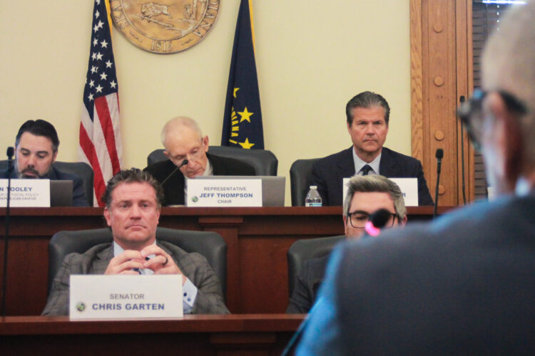 Lawmakers sit in their chairs on two tiers of desks, watching someone speak to them.