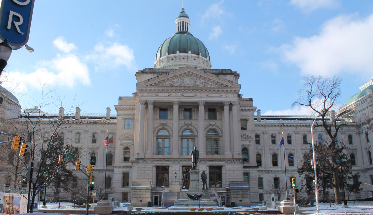 The Indiana Statehouse in winter. There is a little snow on the ground and the Statehouse is in front of a backdrop of blue sky.