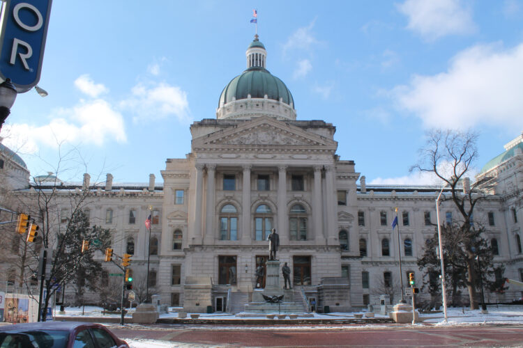 The Indiana Statehouse in winter. There is a little snow on the ground and the Statehouse is in front of a backdrop of blue sky.