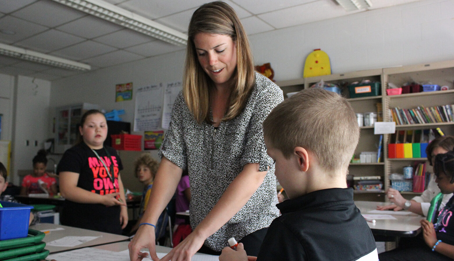 A teacher points to a paper on a student's desk.