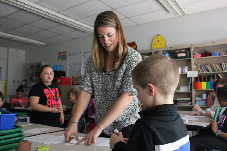 A teacher points to a paper on a student's desk.