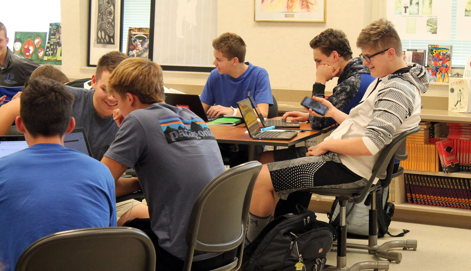 A group of high school students sit in a classroom, working on laptops.