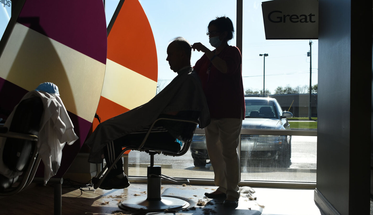 The silhouette of a barber cutting a man's hair.