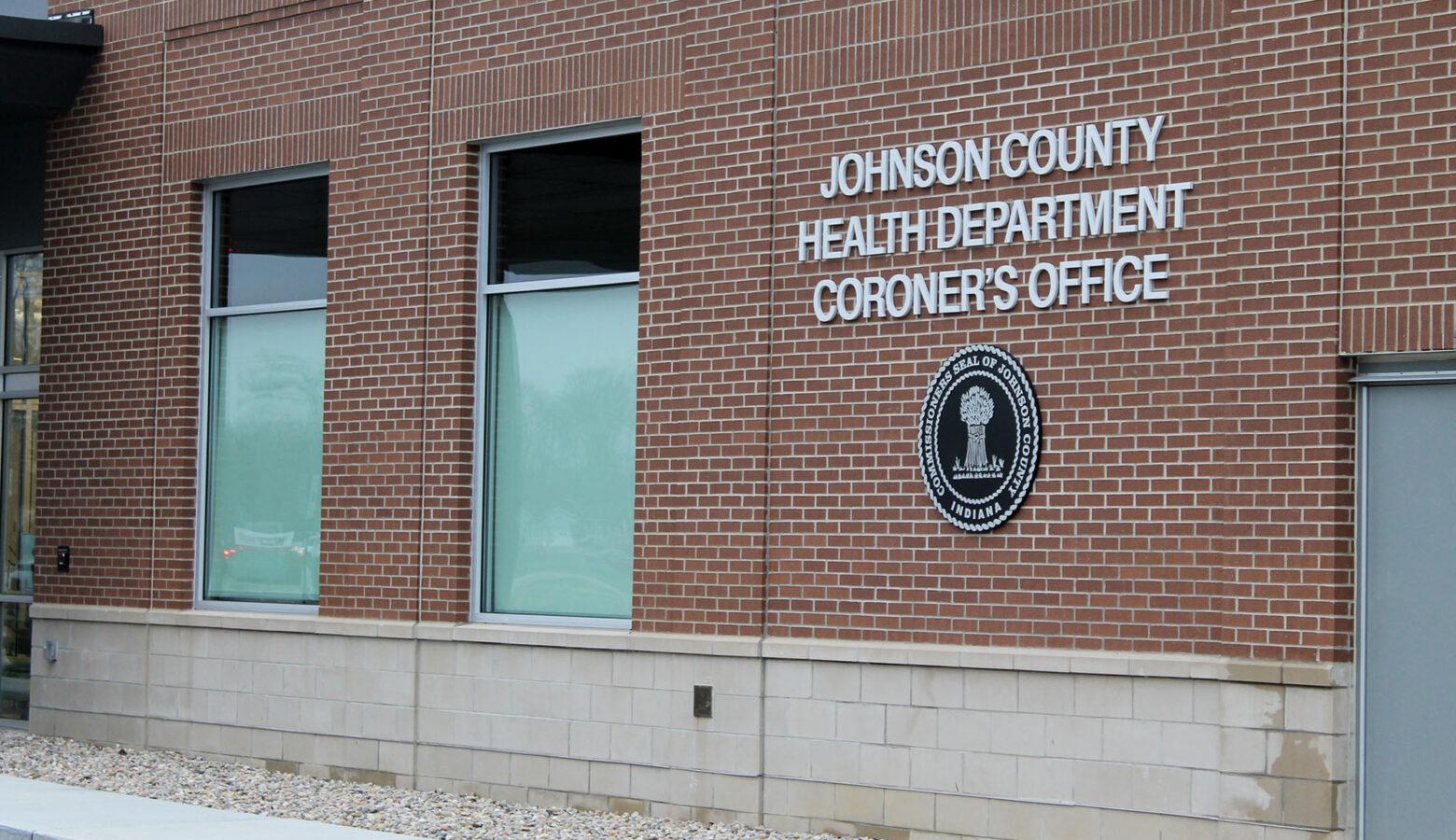 The sign for the Johnson County Health Department and Coroner's Office on the side of a brick building, with the county's seal underneath.