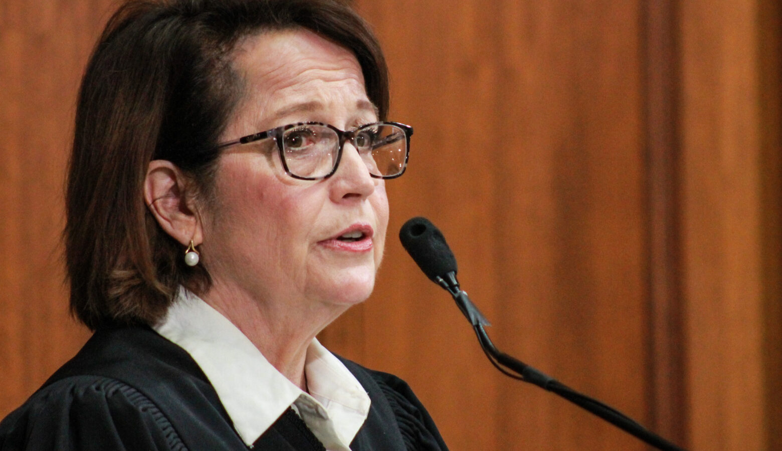 Loretta Rush is a White woman with dark brown hair. She is wearing glasses and black judicial robes over a white shirt.