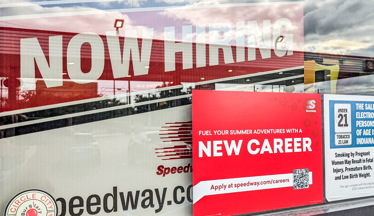 A white and red sign reads "Now Hiring" at the top inside the window. A smaller red sign has bold white letters that reads "New Career."