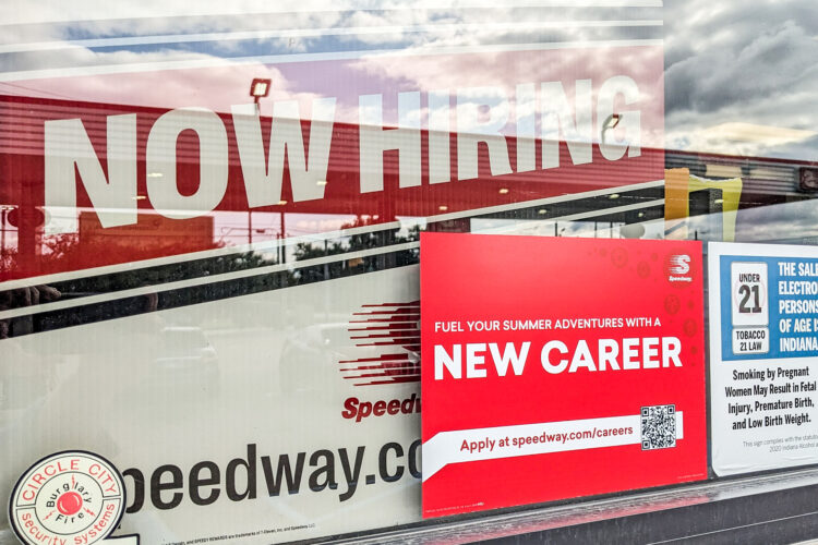 A white and red sign reads "Now Hiring" at the top inside the window. A smaller red sign has bold white letters that reads "New Career."